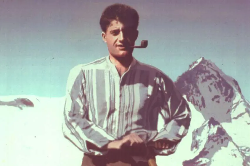 Saint Pier Giorgio Frassati atop a mountain with pipe in mouth, donning a striped shirt