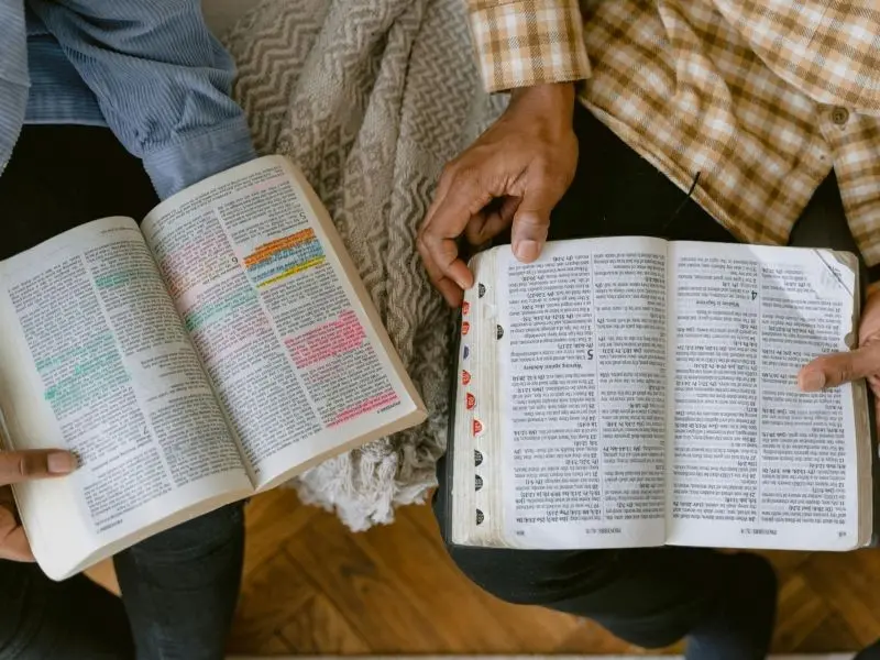Overhead view of two people sitting together, each holding an open and well-studied Bible on their lap.