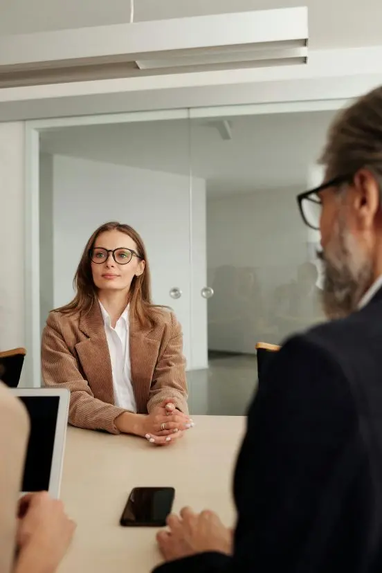 A young woman with glasses sits at a table during a professional meeting.